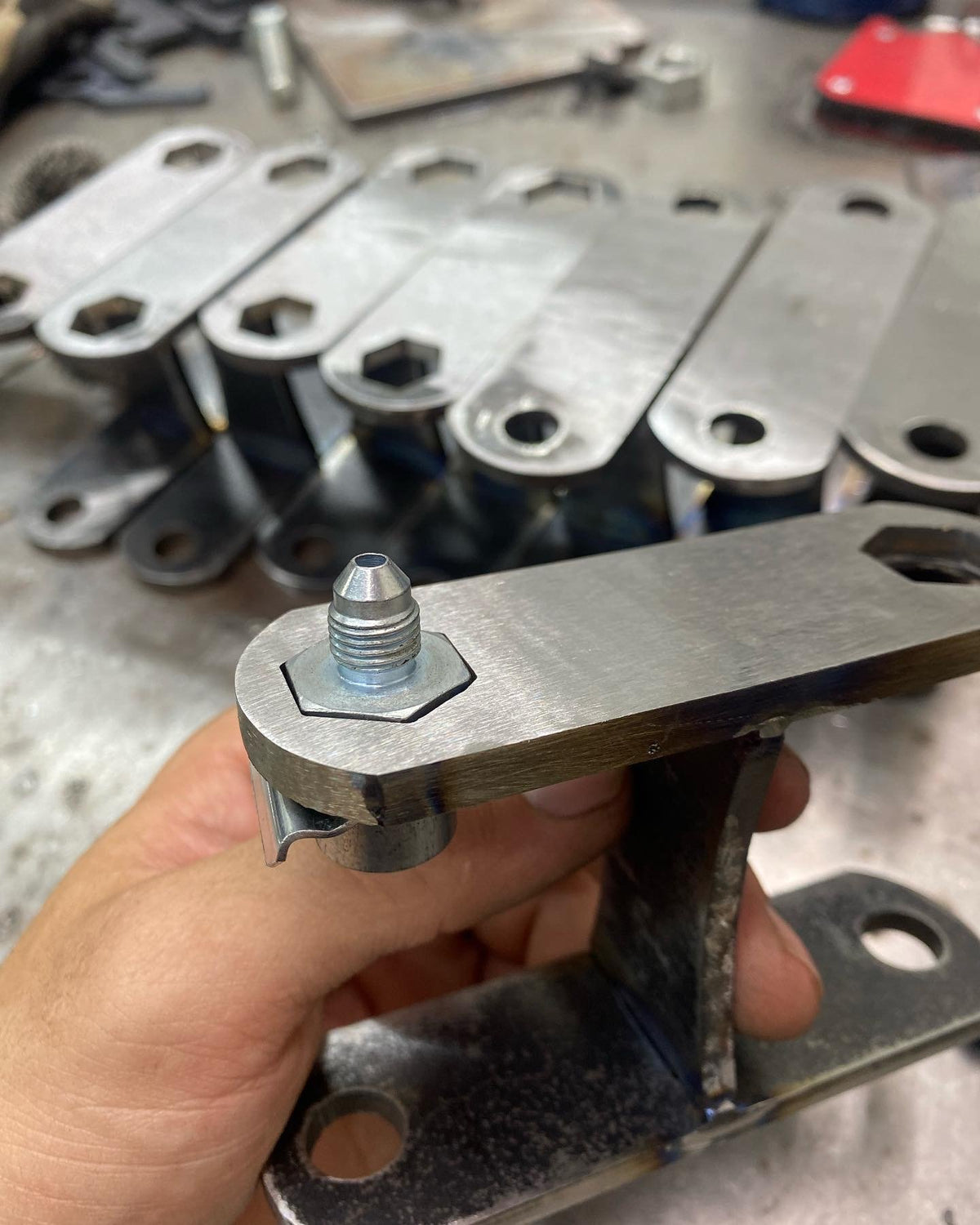 Hand holding a welded bracket with a fitting, more brackets behind