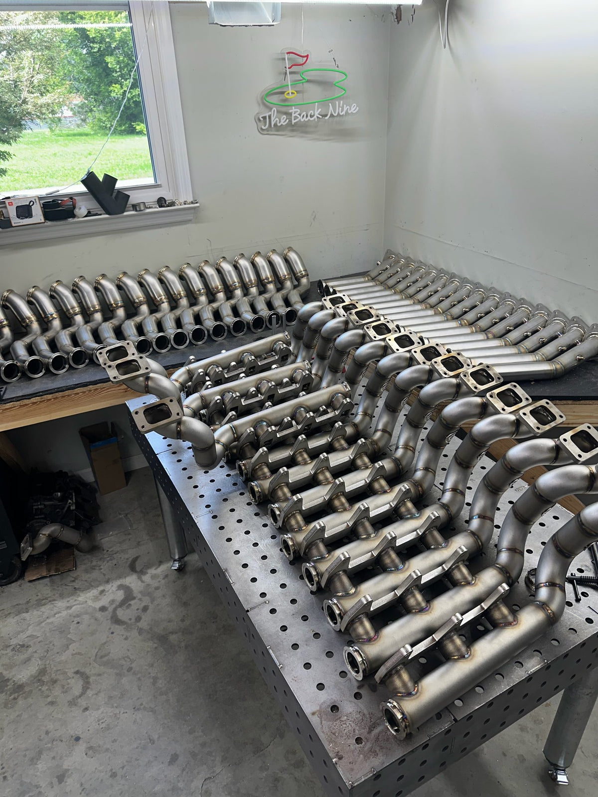 Production batch of fabricated parts on a fixture table in the Tomlin Performance shop